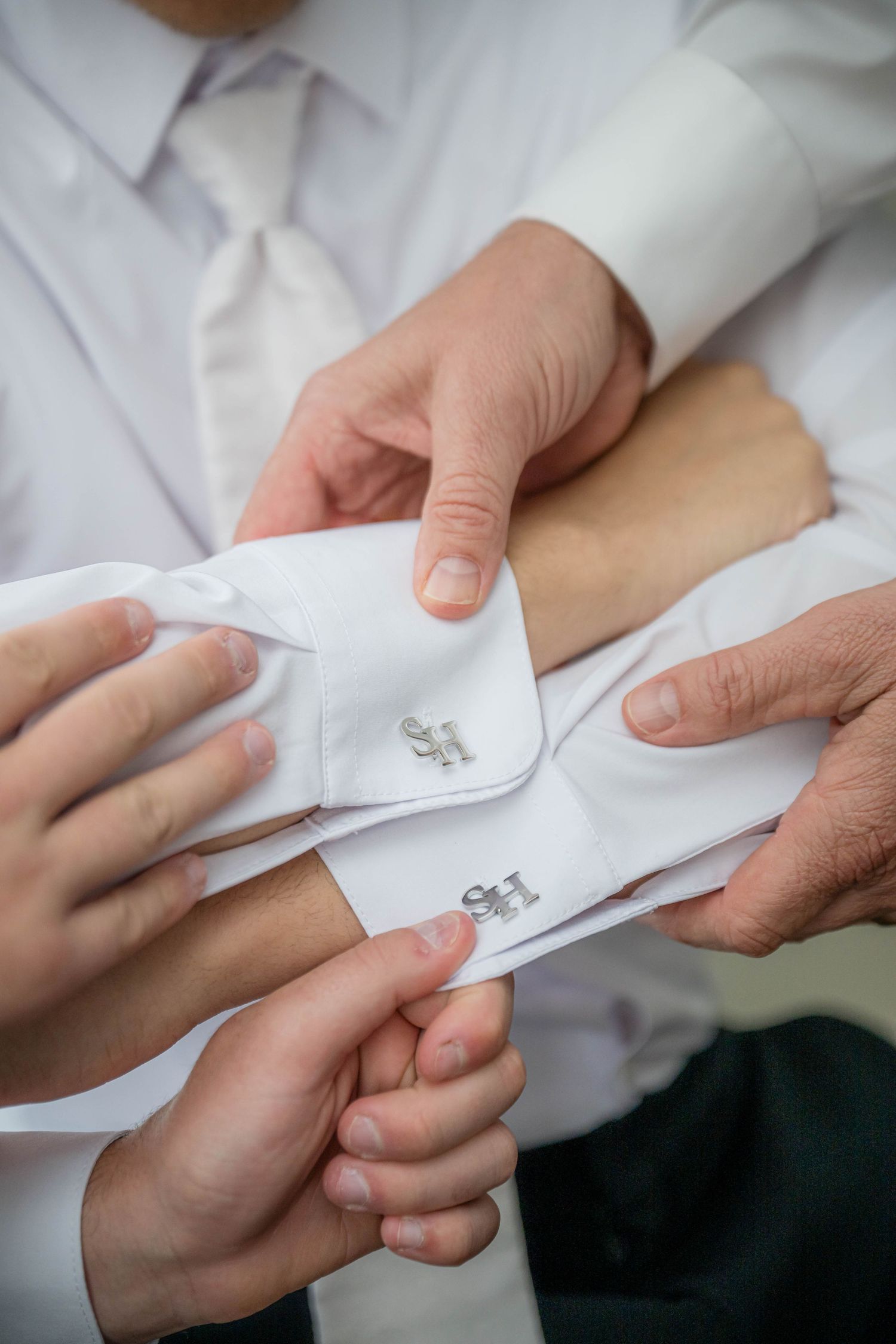 Man's hands adjusting white shirt cuffs and cufflinks in sequence to prepare formal attire for special occasion.