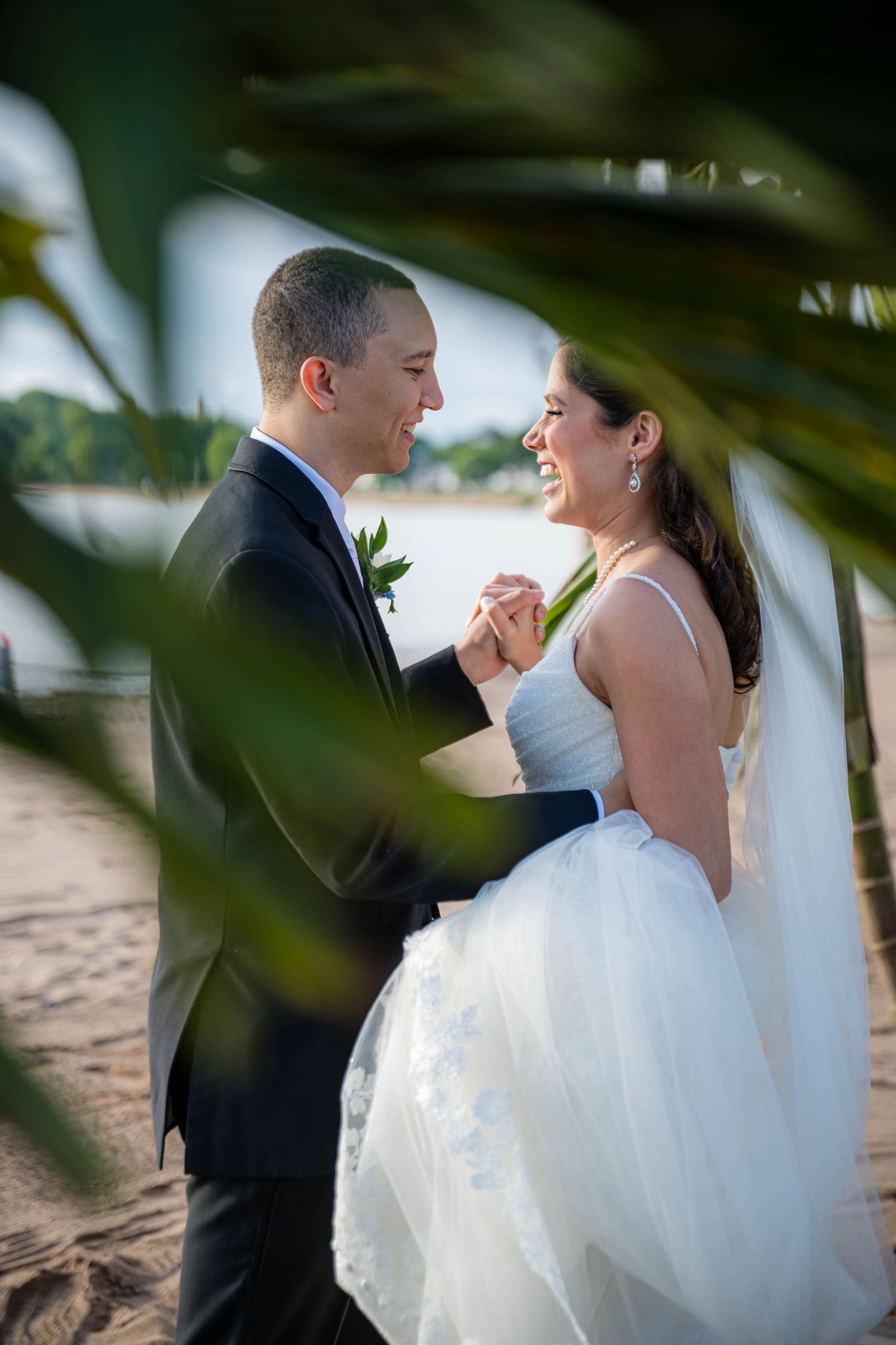 A romantic moment between newlyweds on a tropical beach with palm fronds framing their intimate dance.