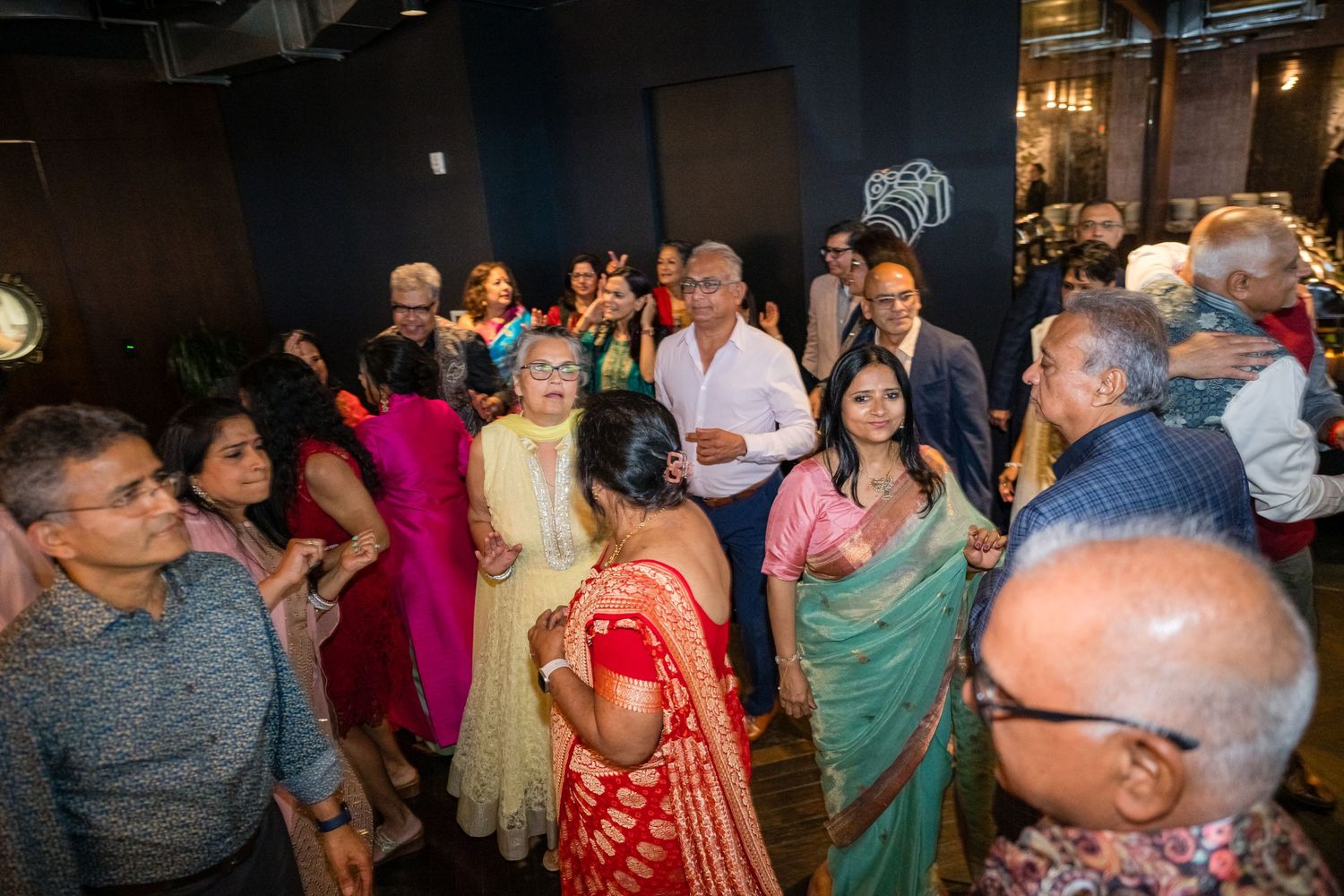 A crowded dance floor shows people in traditional Indian attire celebrating at a festive cultural event.