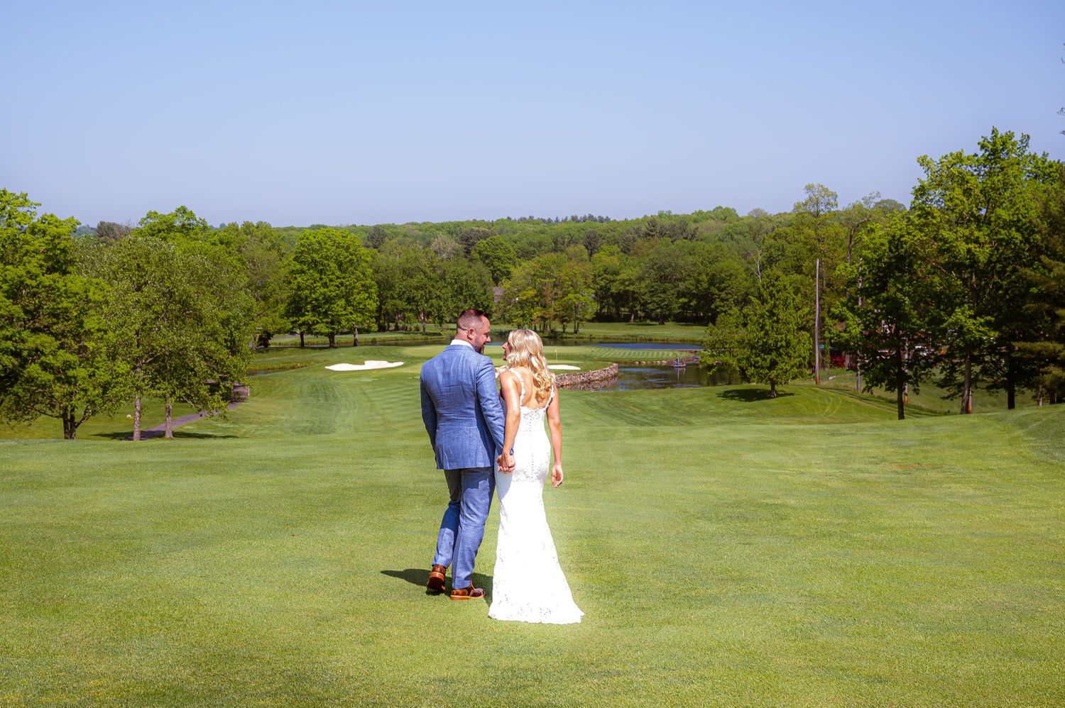 Couple standing together on a lush green golf course overlooking the landscape on their wedding day.