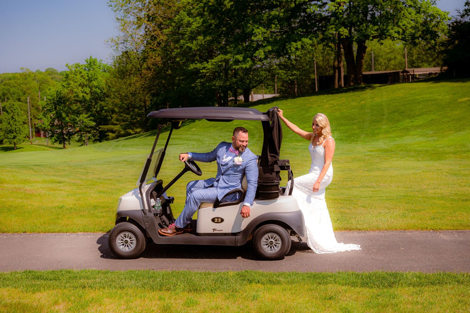 A couple on a golf course walking alongside a golf cart on a sunny summer day with lush green slopes.