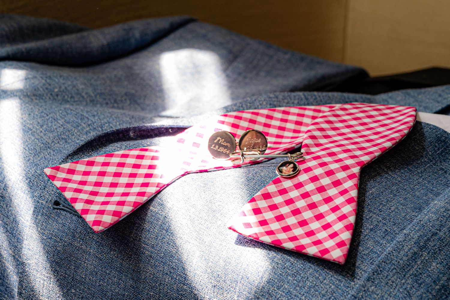Two metal buttons rest on a red and white checkered fabric against a dark textile background in sunlight.
