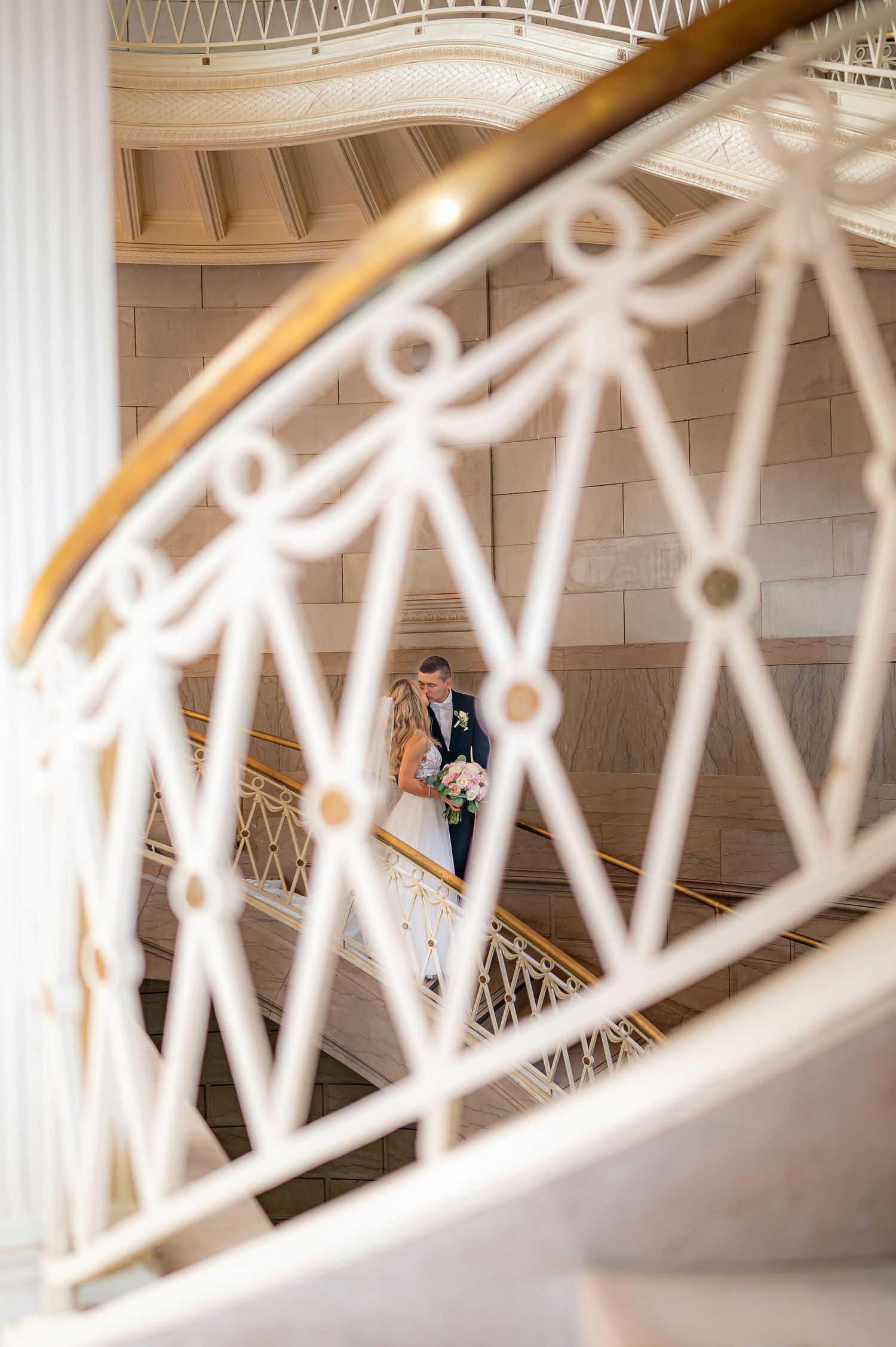 Wedding couple stands on a spiral staircase with elegant white railings creating a romantic architectural frame.