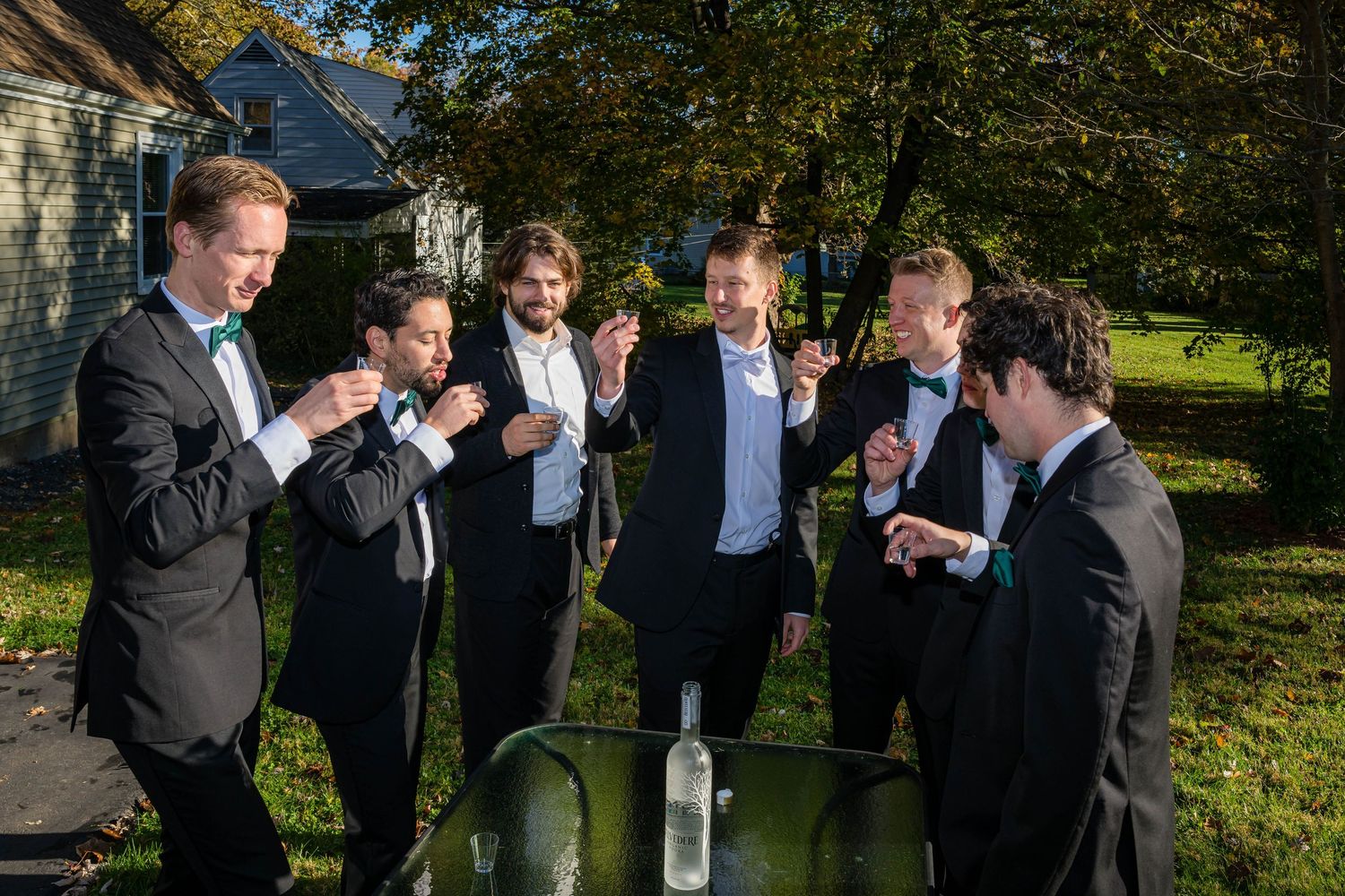 A group of formally dressed people gather outdoors on a sunny day for a celebratory moment in a garden setting.
