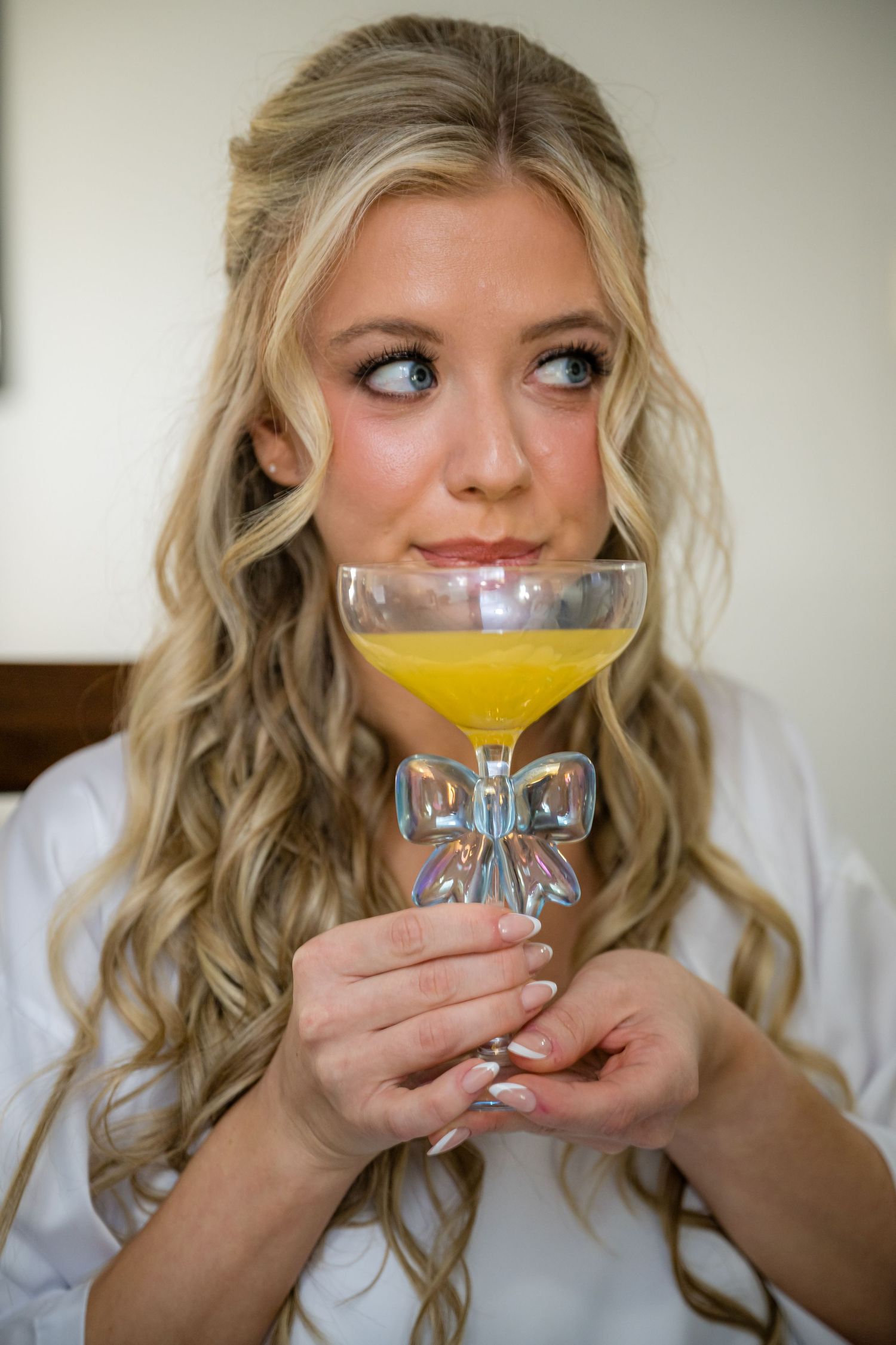 A person in a white top holds and sips from a coupe glass filled with a yellow cocktail in a sequence of photos.