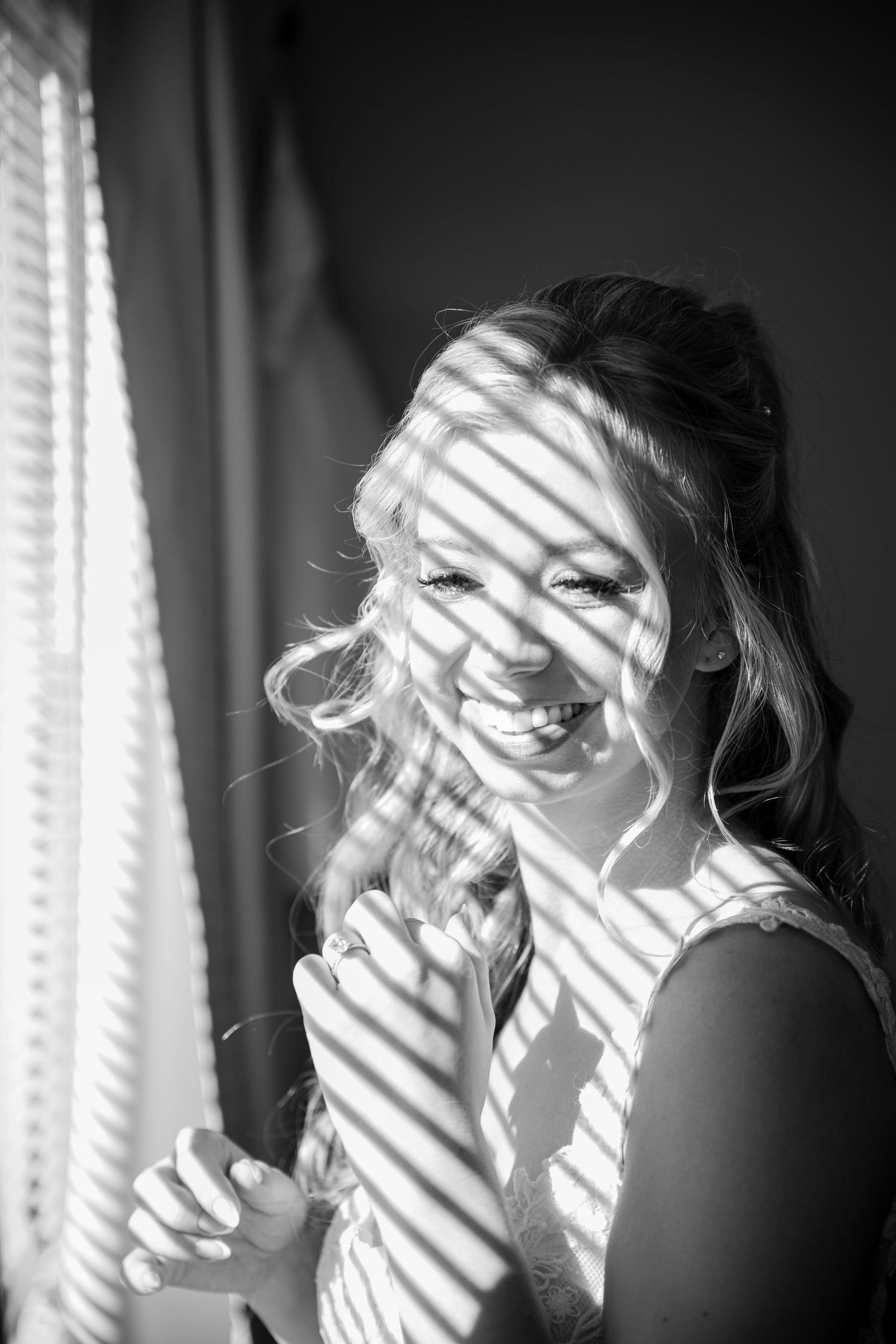 Black and white portrait with dramatic window blind shadows creating stripes across a joyful expression.