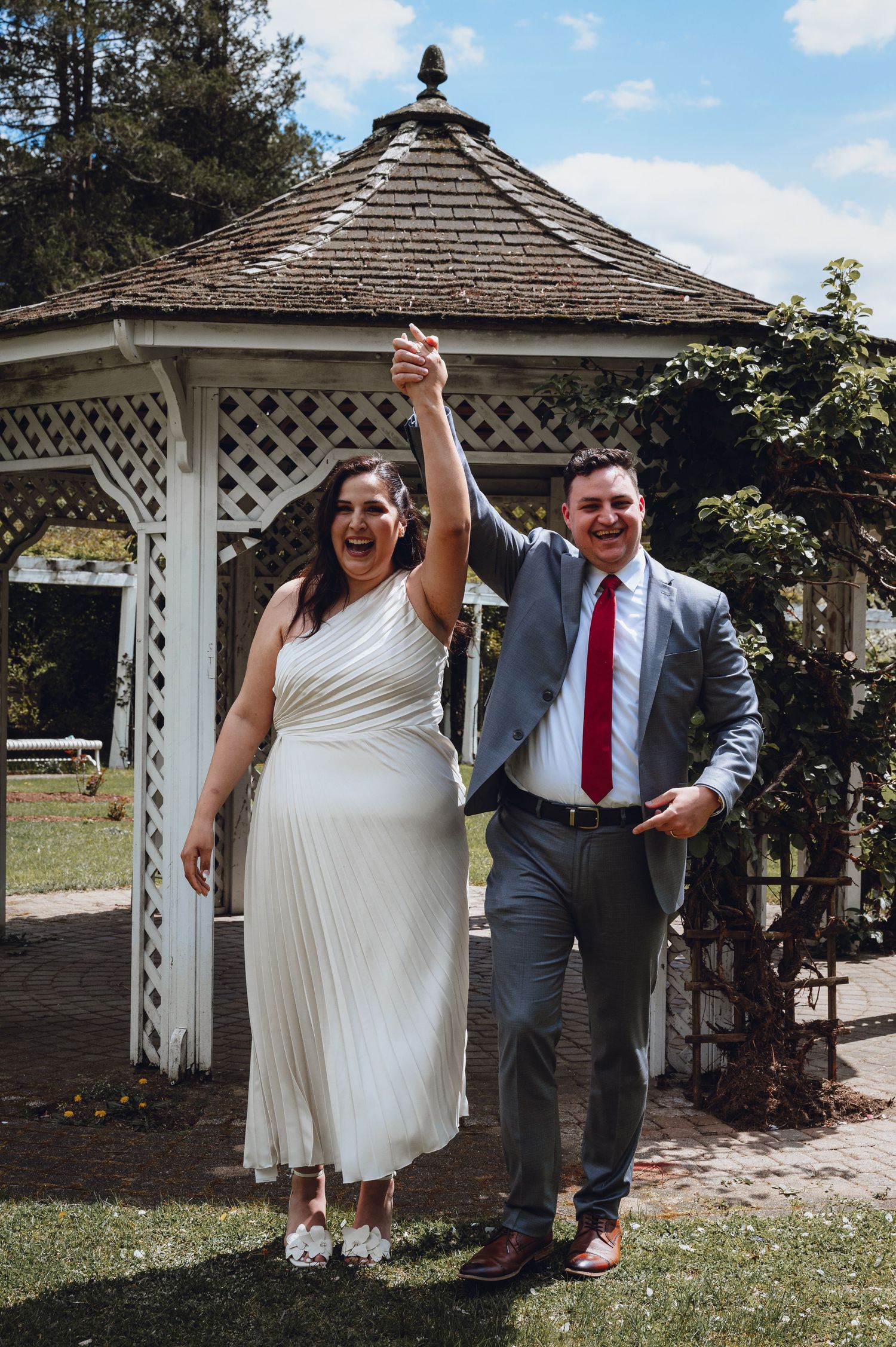 Wedding couple celebrating under a white wooden gazebo in a garden setting.