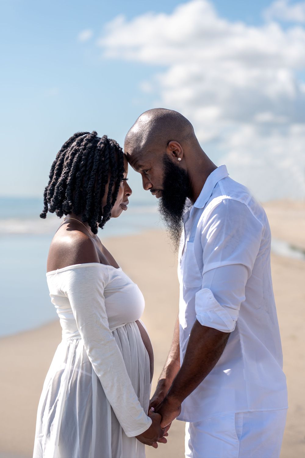 Intimate couple in white clothing shares tender moments against beach backdrop.