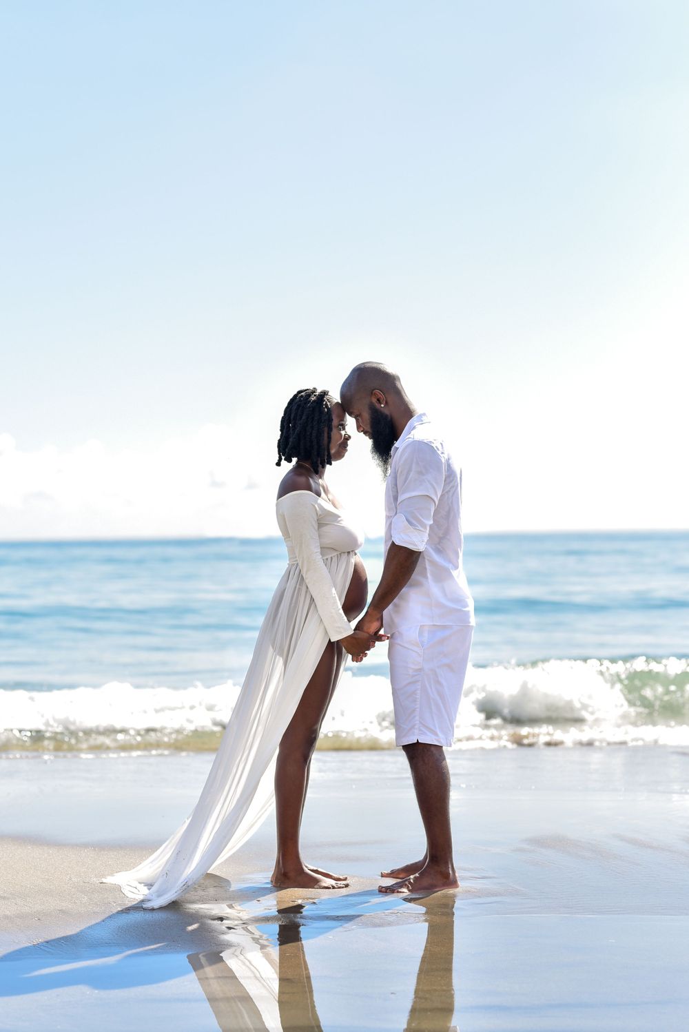 Couple holds hands while standing in gentle ocean waves at beach.