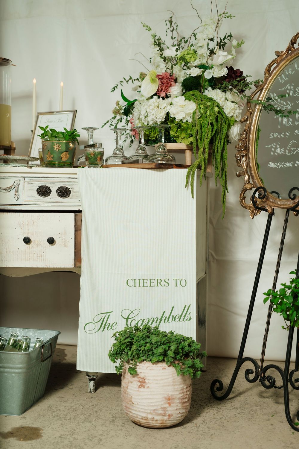 Elegant wedding bar setup with floral arrangement, candles, and a personalized "Cheers to The Campbells" banner.