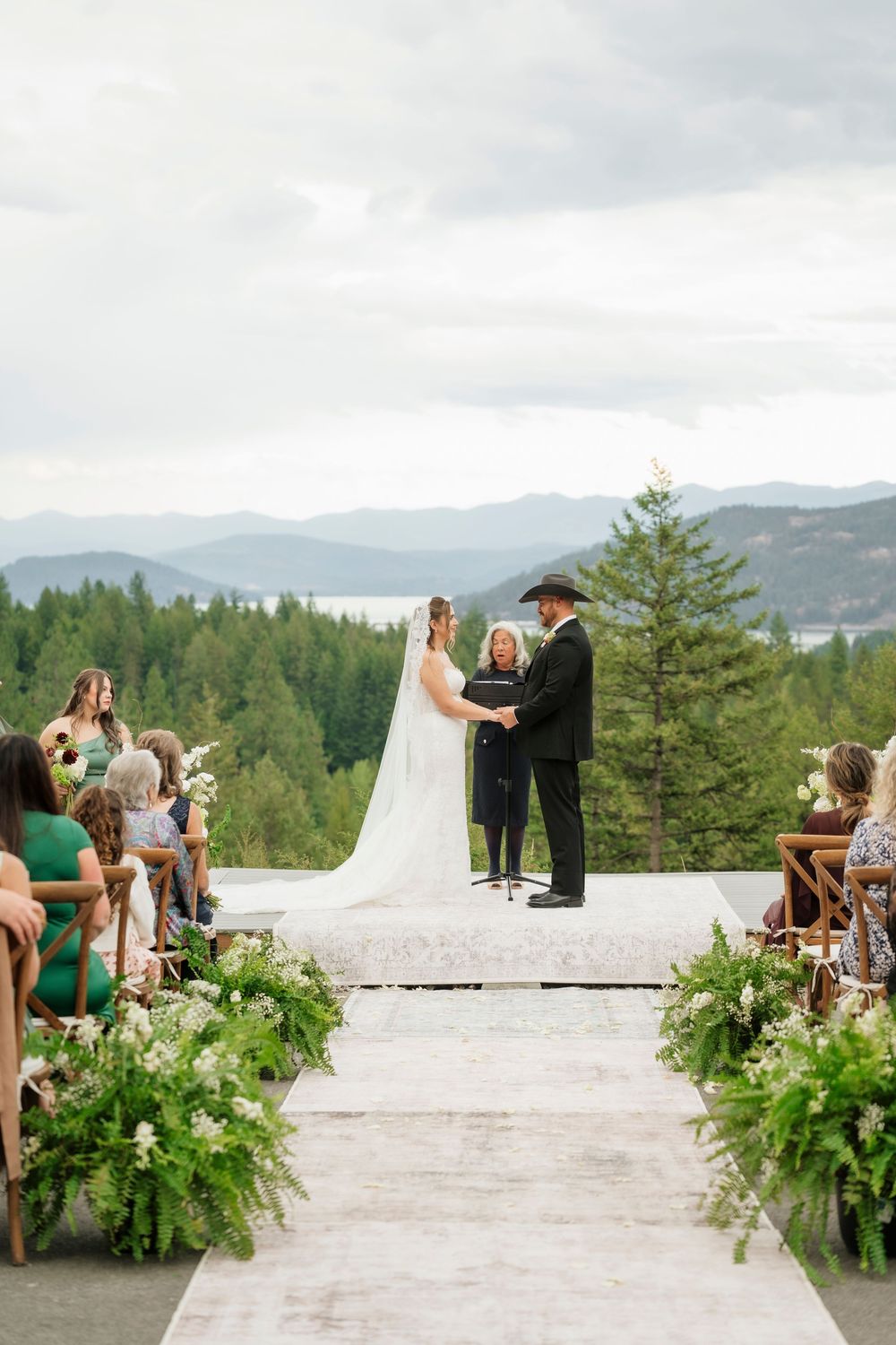 Bride and groom exchange vows at outdoor mountain wedding ceremony with lush greenery aisle decor.
