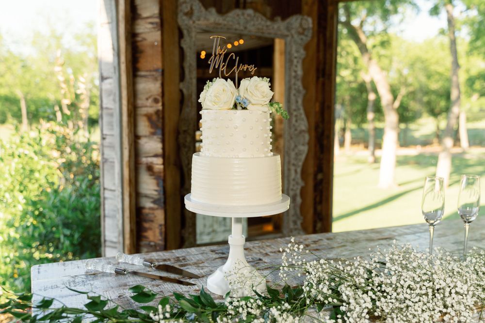 Rustic wedding cake display with white flowers and greenery on wooden table.