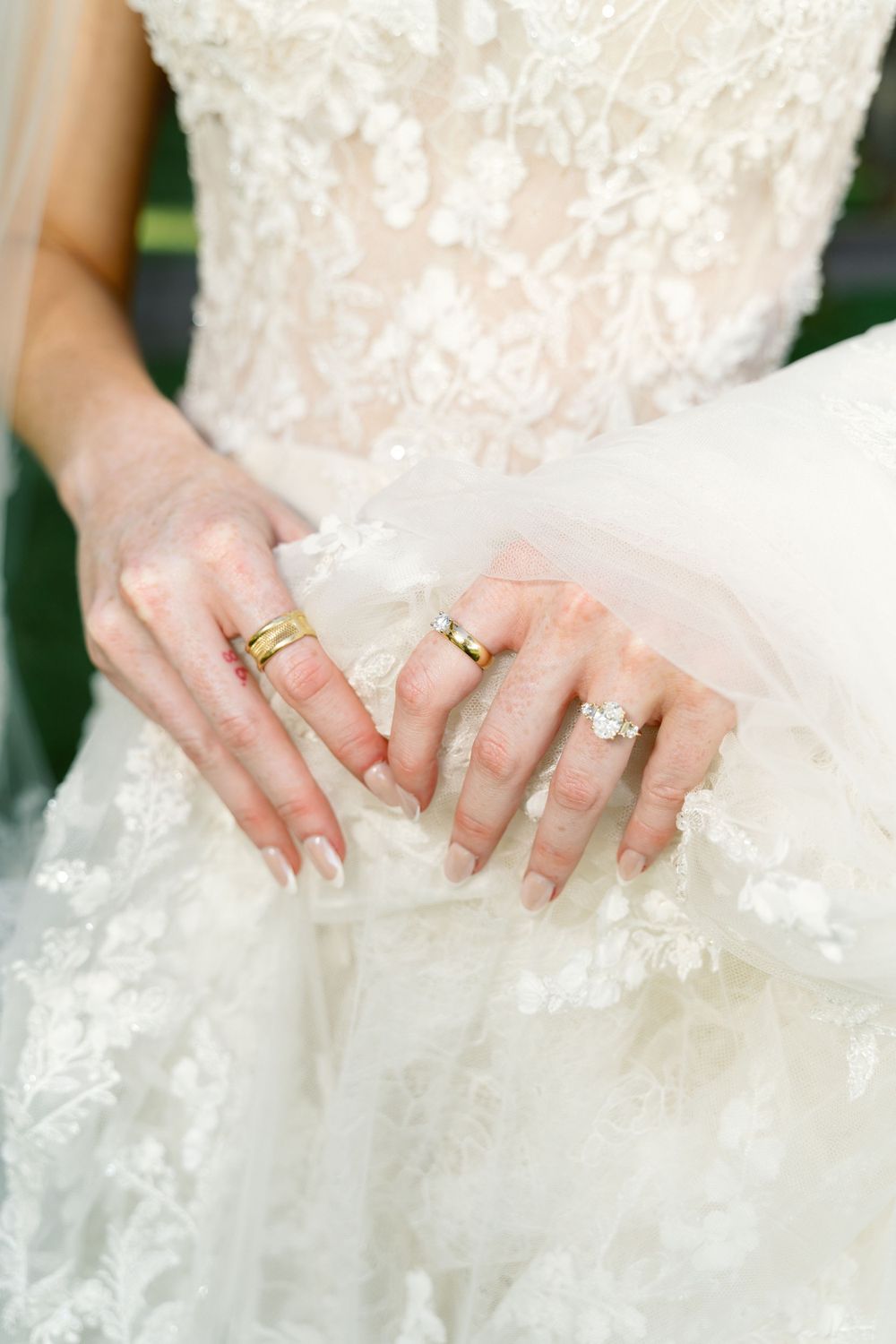 Close-up of hands holding delicate lace wedding dress fabric with rings visible.