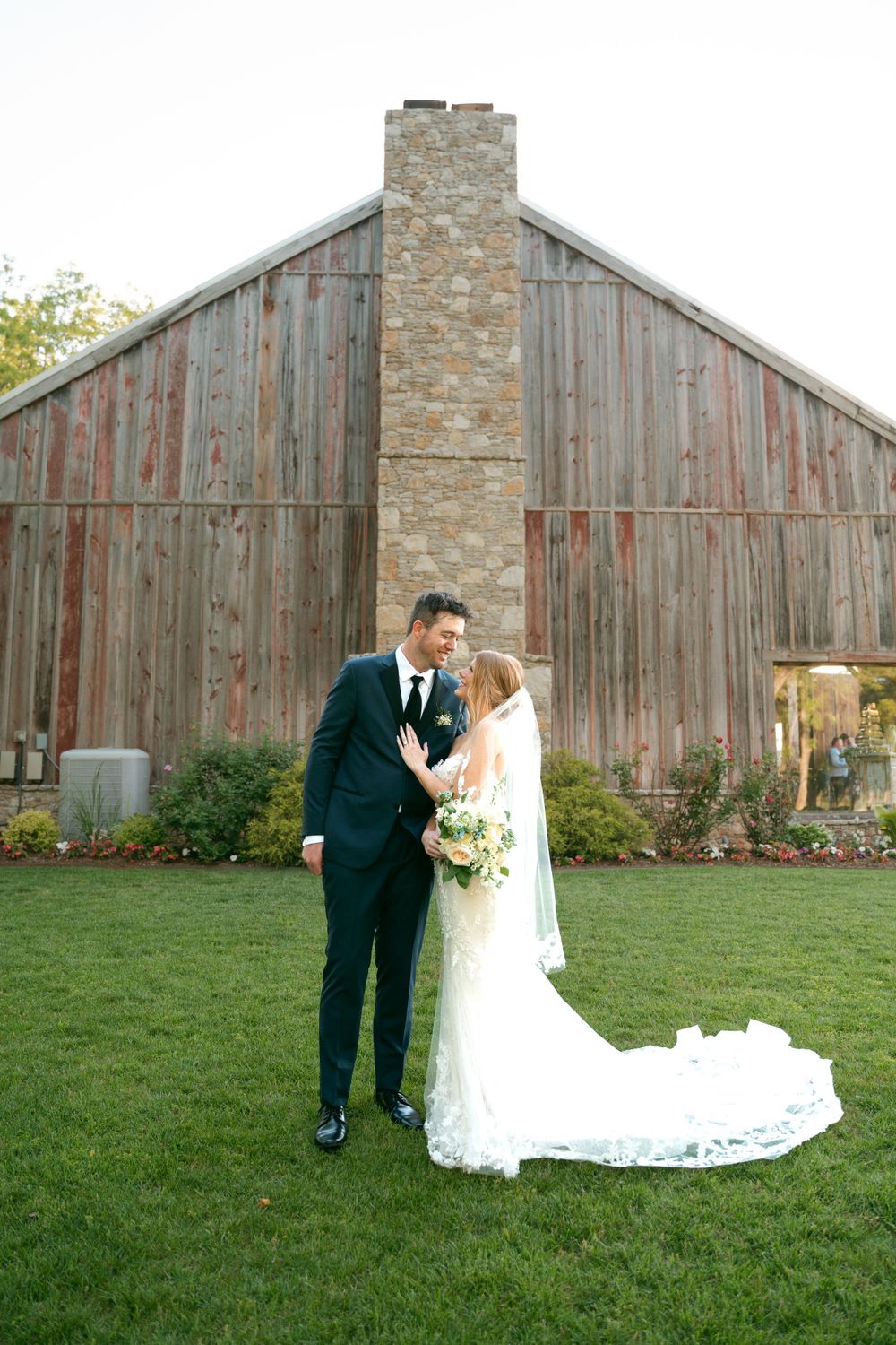Newlyweds share a moment in front of rustic wooden barn.