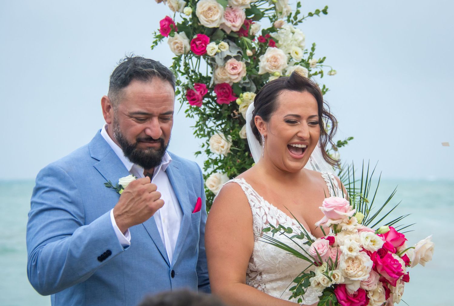 Emotional bride and groom sharing a heartfelt moment during outdoor beach wedding ceremony with floral arch.
