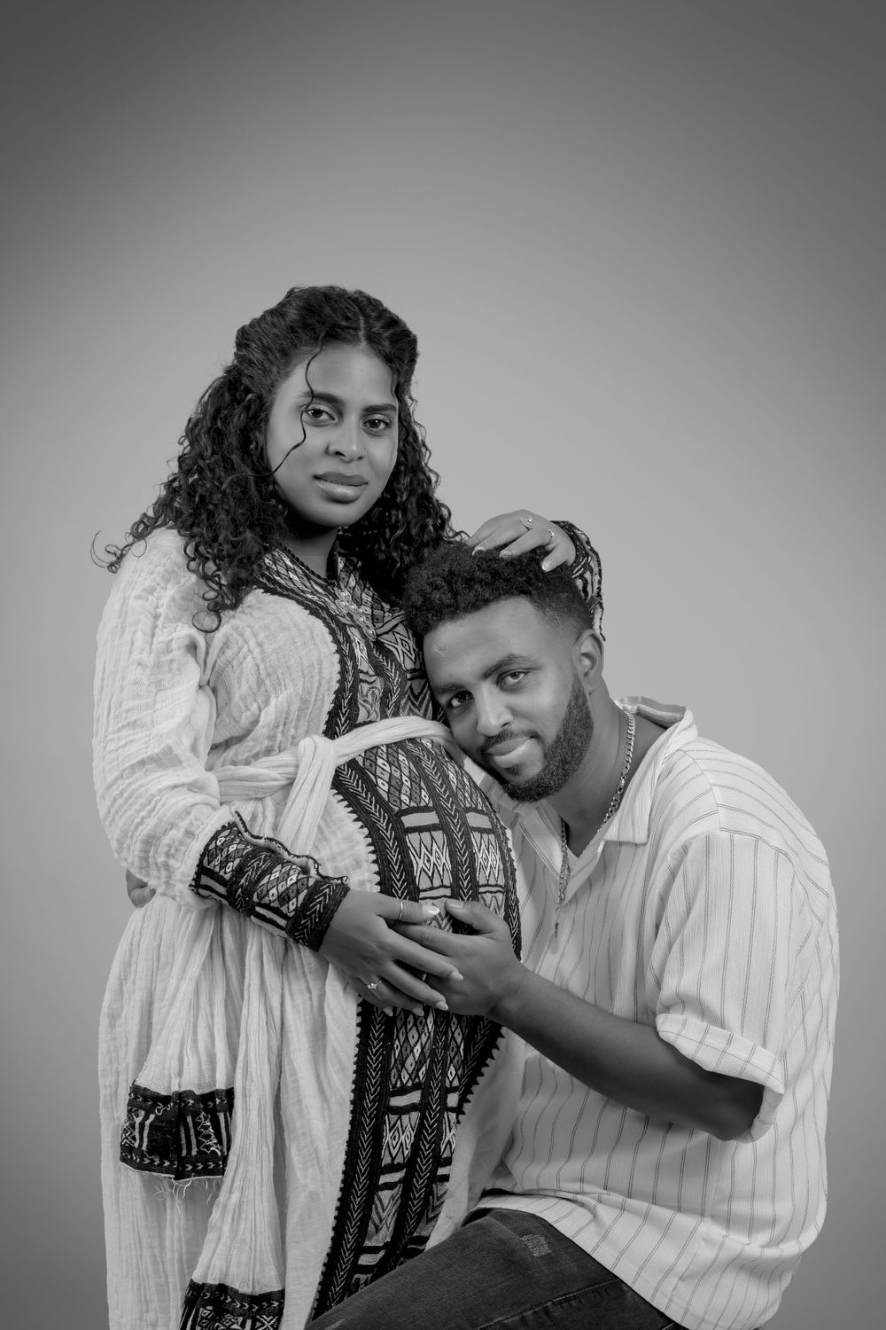 Black and white maternity portrait with couple in traditional ethnic attire.