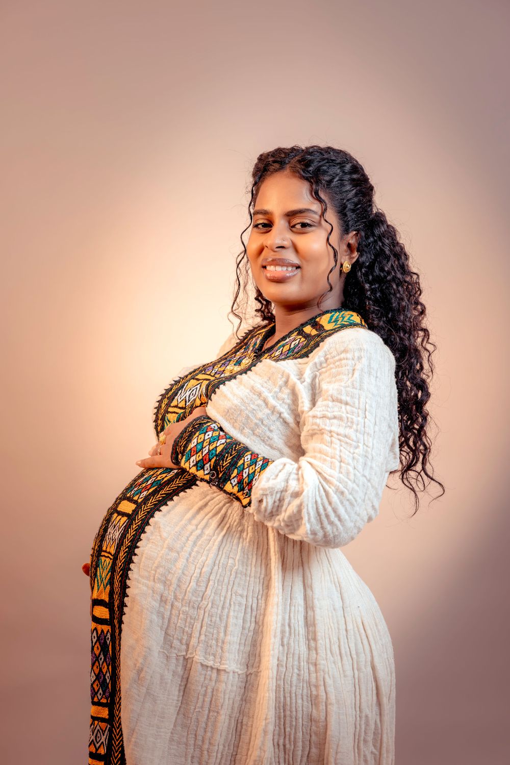 Maternity portrait featuring woman in white dress with ethnic print trim.