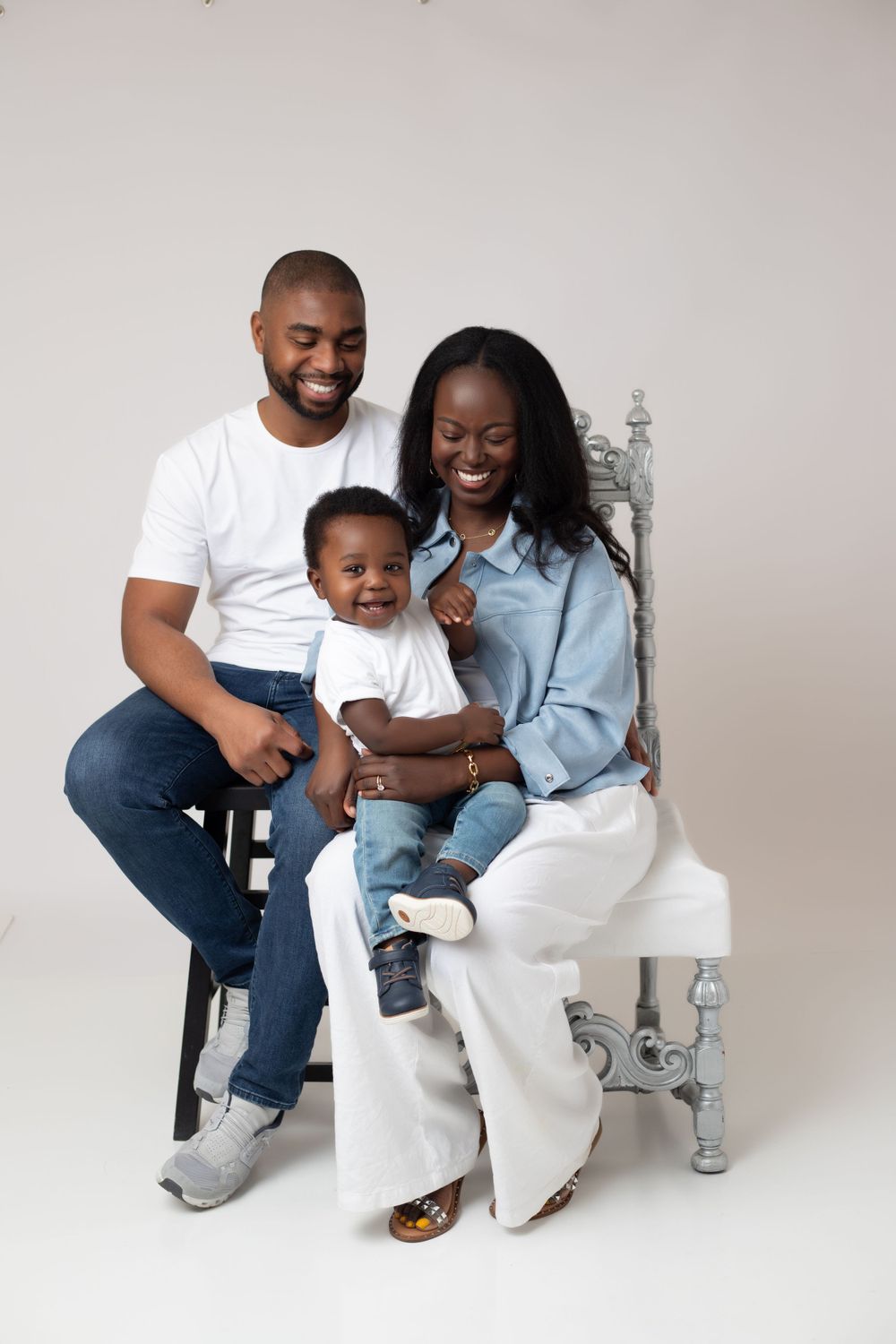 A family wearing coordinated white and denim outfits poses together for professional studio portraits against a white backdrop.