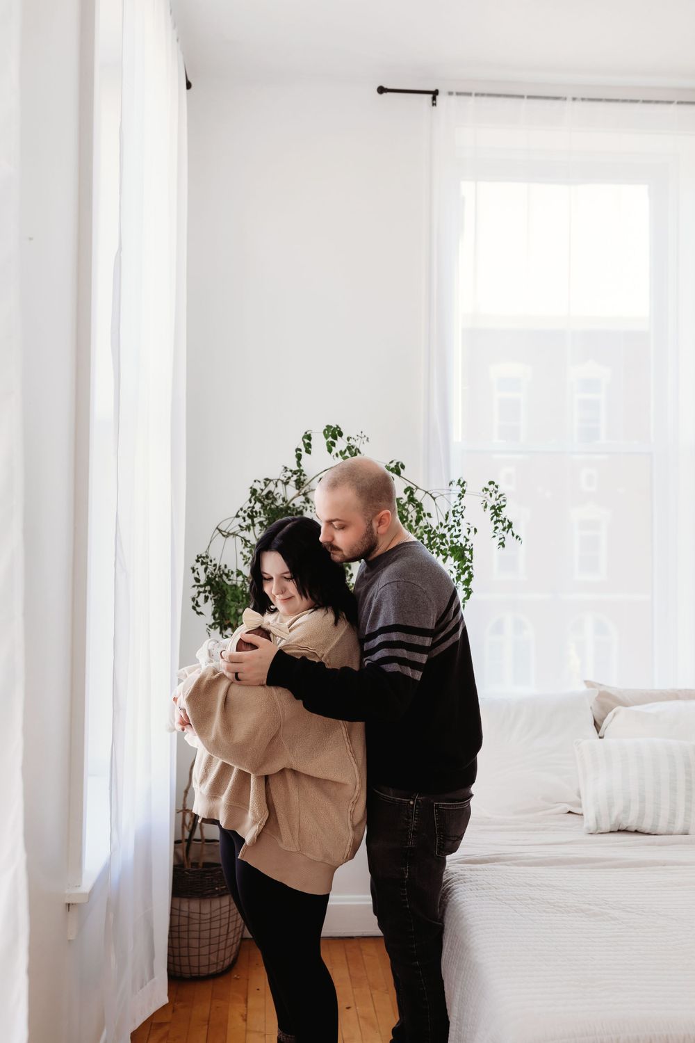 A couple embraces in a bright minimalist room with white walls and natural light streaming through the window.