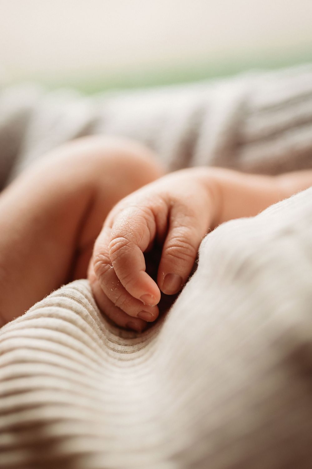 A close-up view of a tiny baby's fingers grasping white fabric in soft natural lighting.