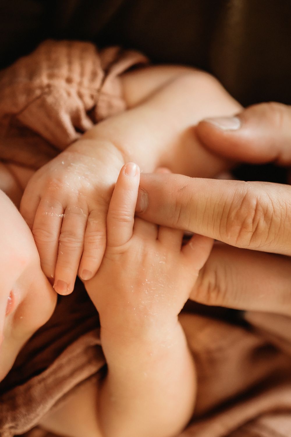 A series of close-up shots showing tiny baby hands grasping adult fingers in warm lighting.