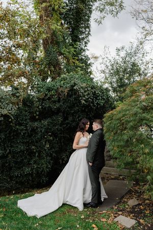 A couple shares an intimate moment in a lush garden setting with autumn leaves falling around them.