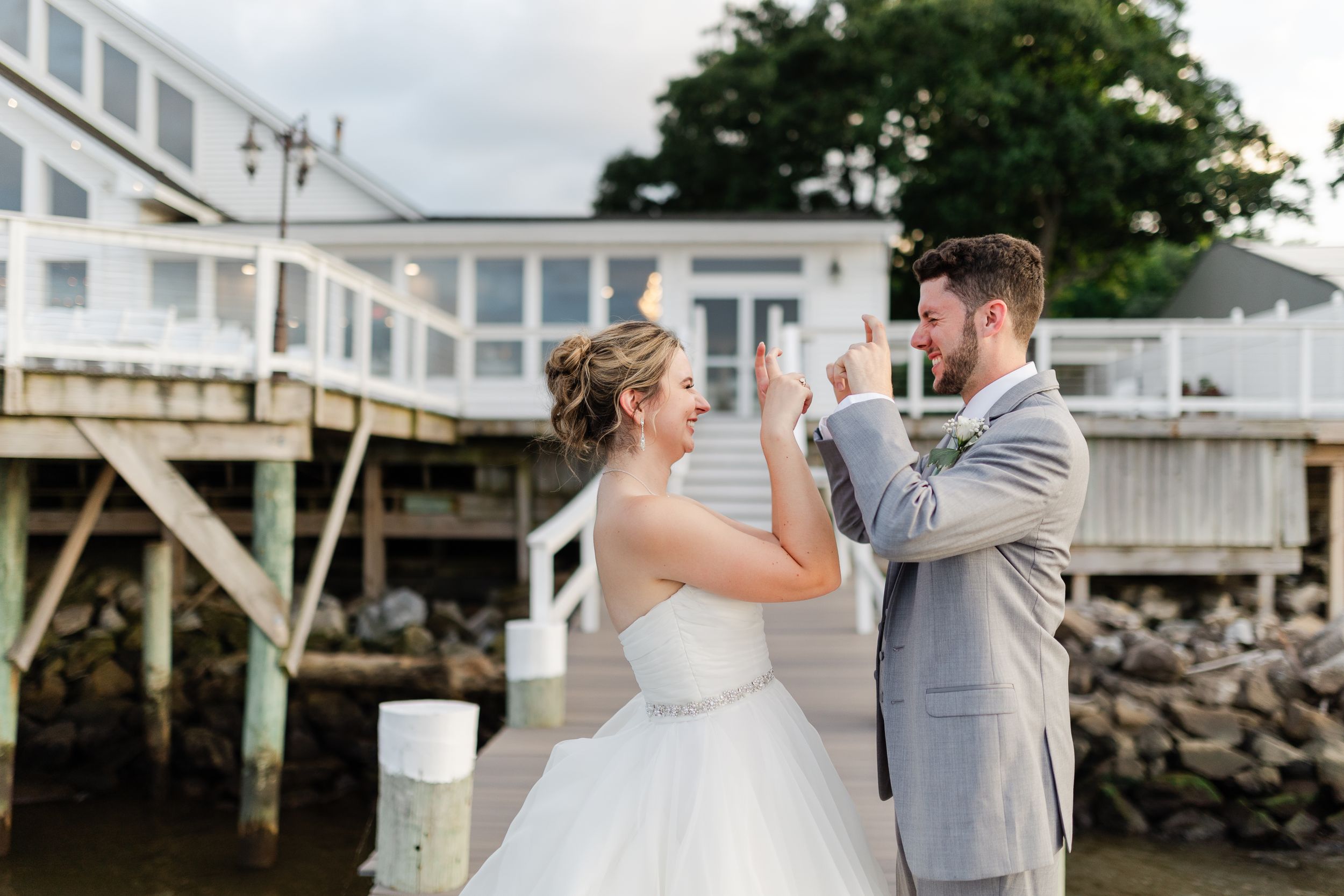 Couple sharing joyful moment on waterfront deck during wedding celebration.