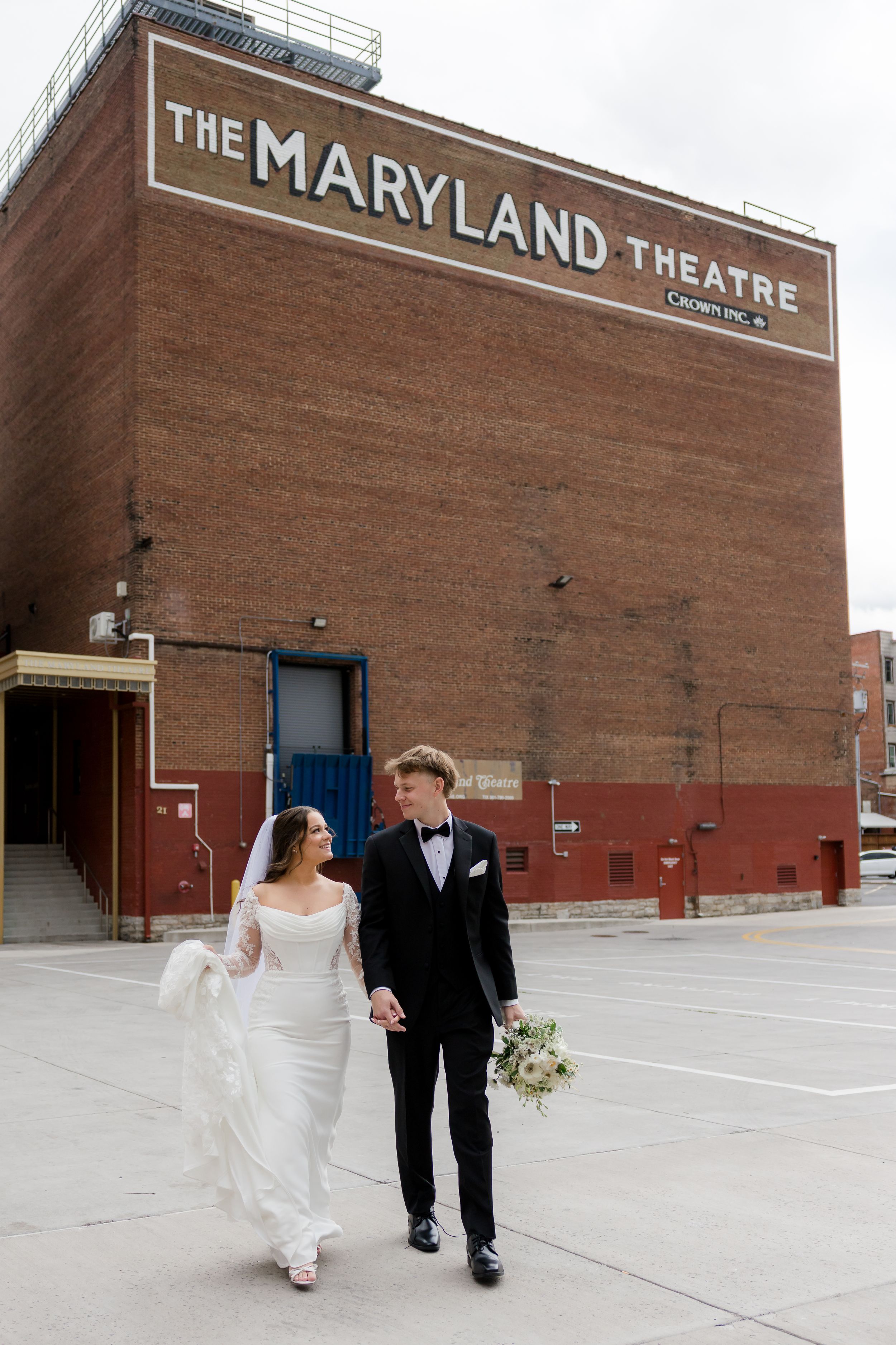 Bride and groom walking hand in hand outside The Maryland Theatre, bride in white gown, groom in black tuxedo.