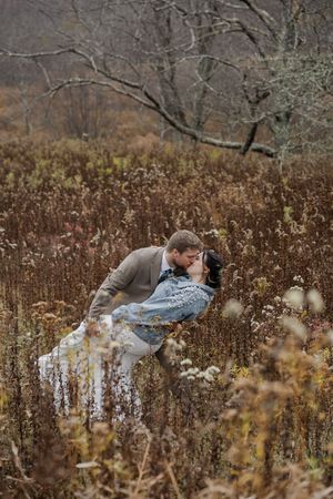A couple shares an intimate moment while lying in a field of tall dried grass and autumn foliage.
