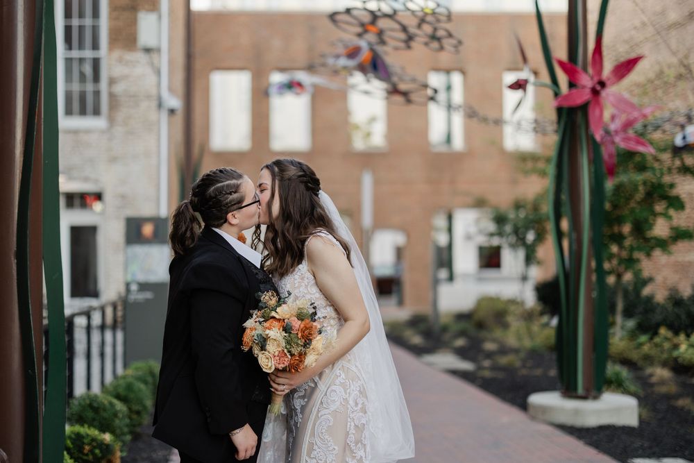 Bride and groom share a romantic kiss on a cobblestone street with brick buildings in the background.