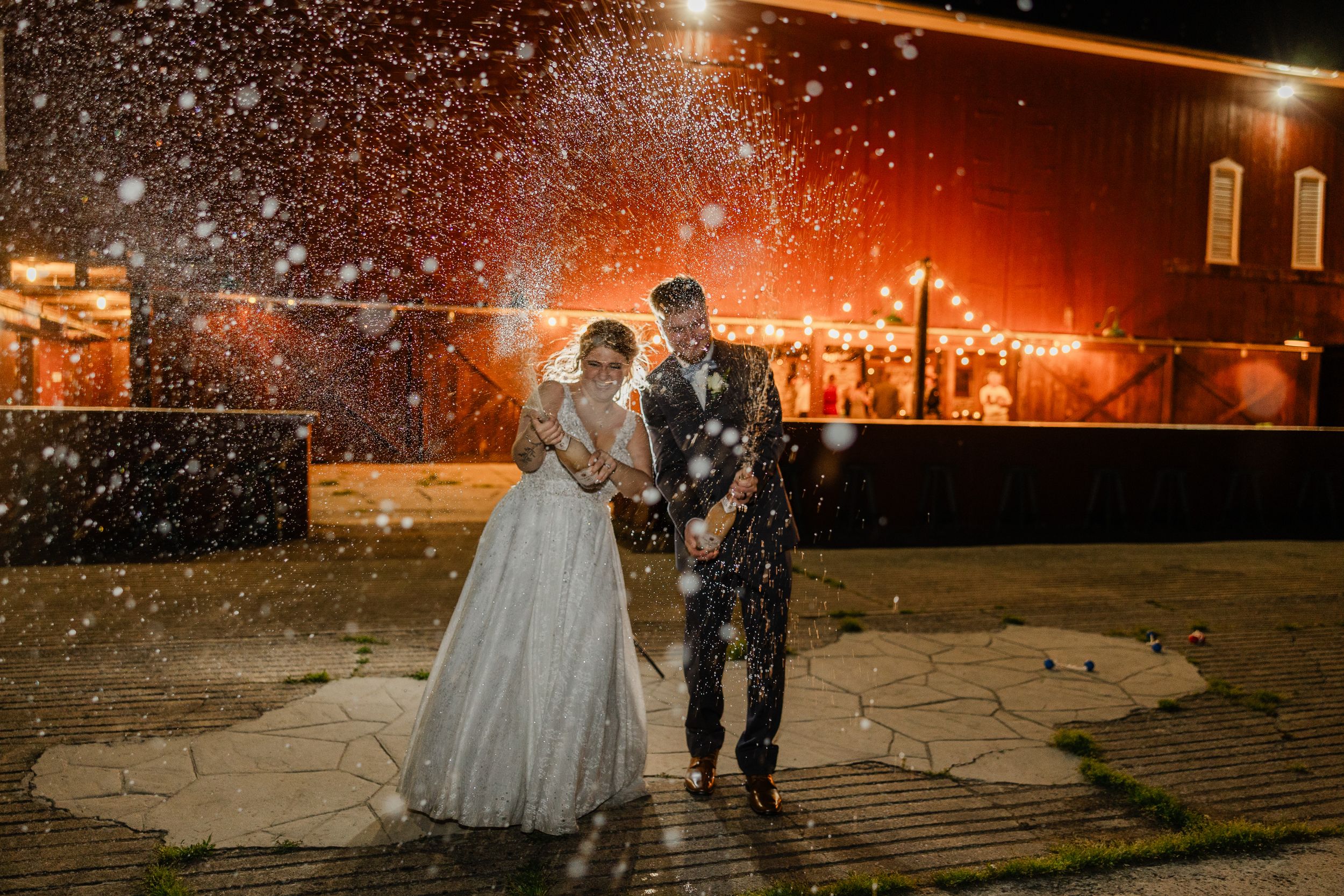 A couple poses in wedding attire while snow falls around them at night.