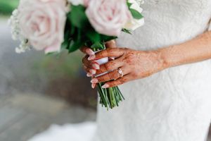 Close up of hands holding a delicate pink rose bridal bouquet with wedding ring visible on finger.