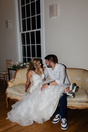 Bride and groom sitting together on a vintage sofa, sharing an intimate moment in a softly lit elegant venue.