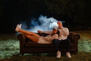 A person lounges on a brown leather couch outdoors at night surrounded by atmospheric smoke effects.
