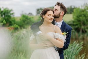 A romantic wedding couple embraces in a garden meadow with soft blurred edges and natural greenery in the background.