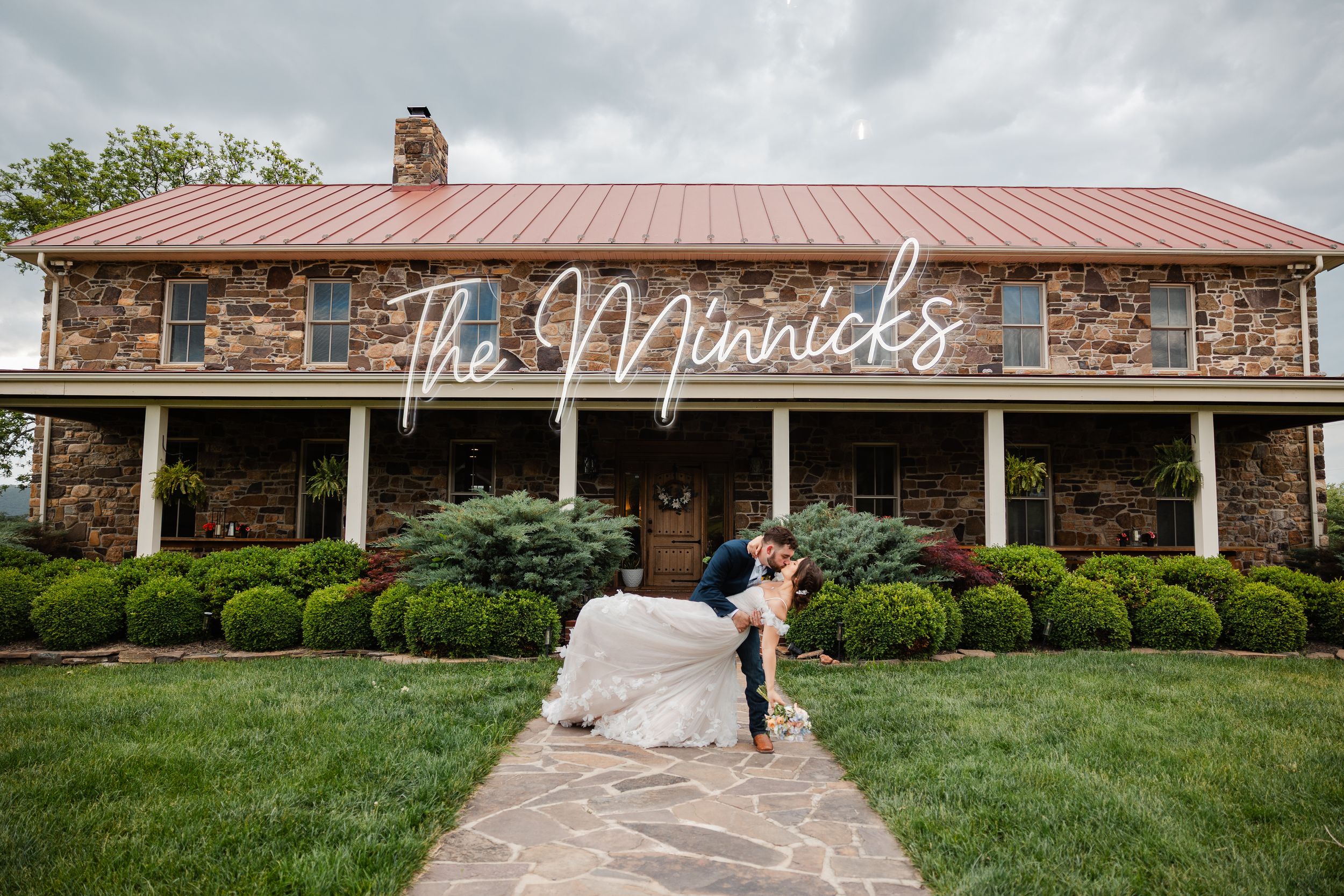 A rustic stone venue with red metal roof and manicured landscaping features The Merricks signage on its facade.