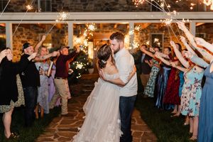 Newlyweds share romantic evening dance while guests hold sparklers creating magical archway in rustic barn venue.