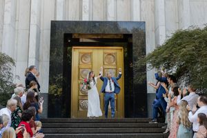 Wedding party and guests gather around ornate gold doors at temple entrance during outdoor ceremony celebration.