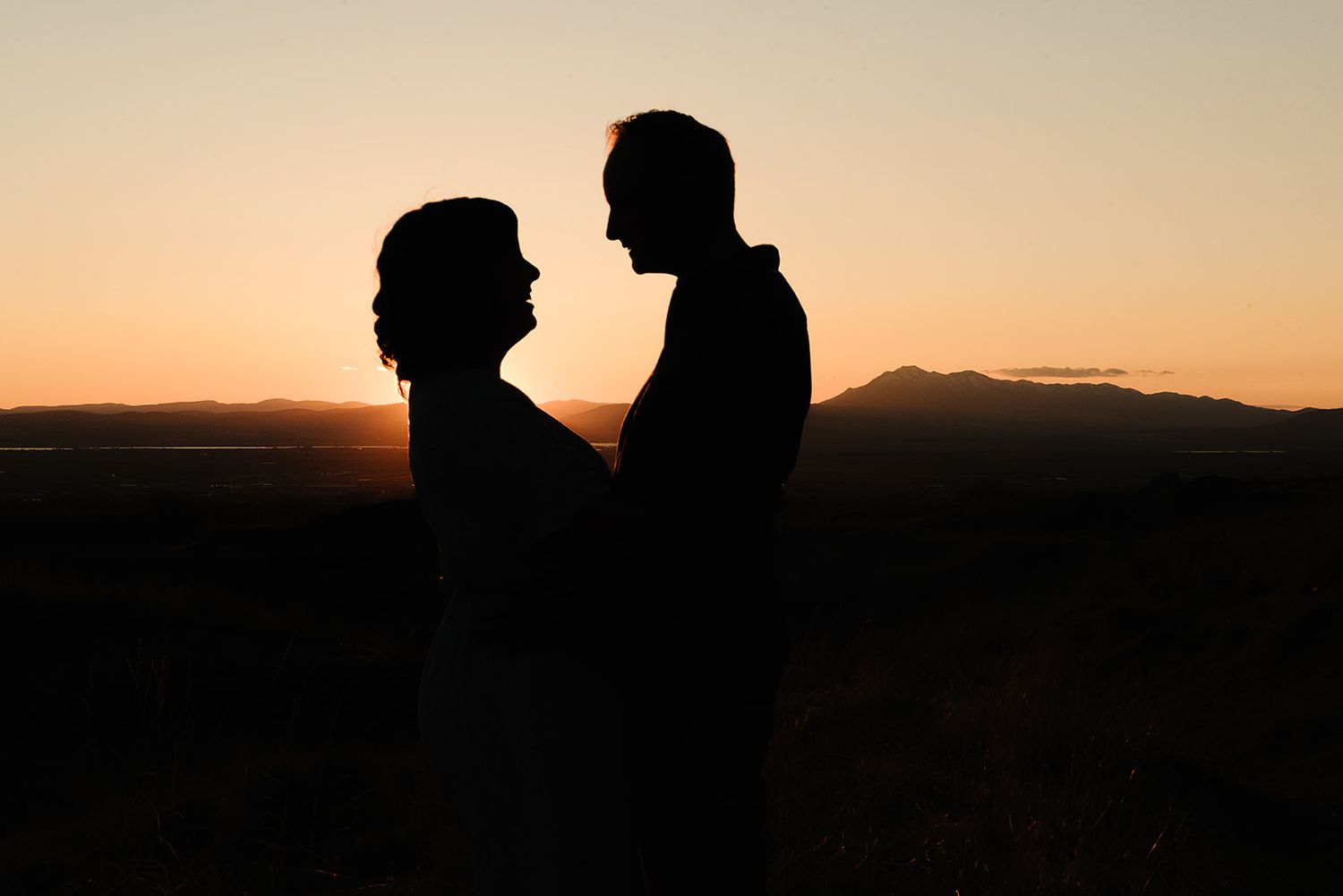 Silhouette of couple against mountain sunset sky in romantic pose.