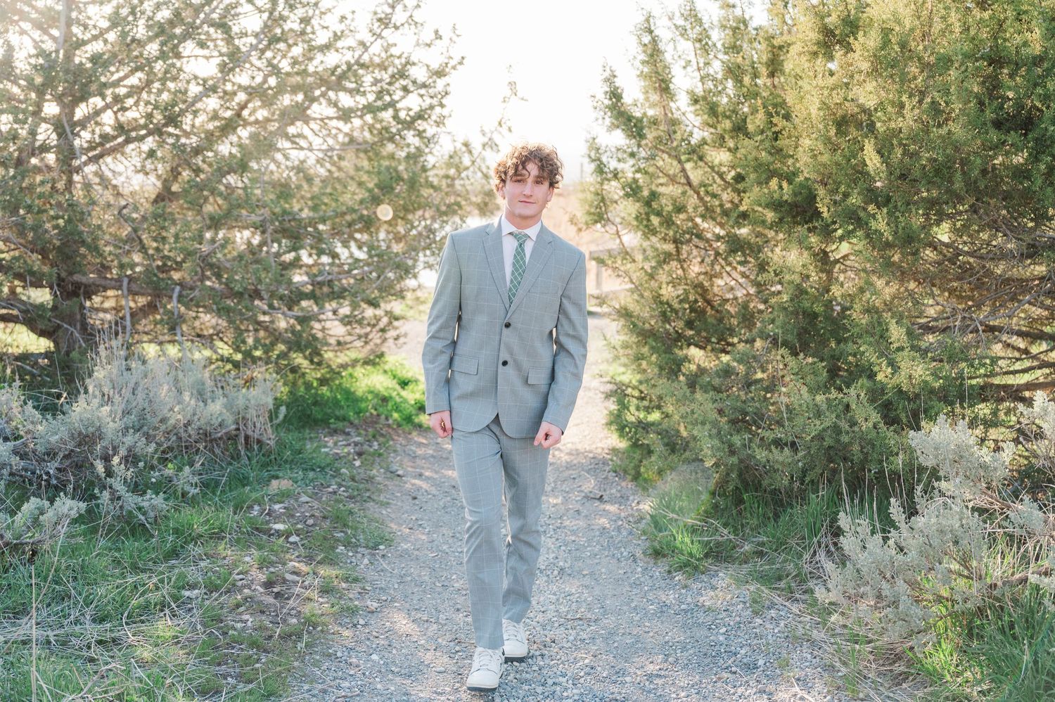 Man in gray suit walking on gravel path surrounded by desert brush.