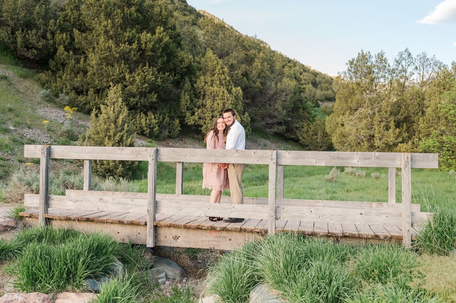 Couple shares intimate moment on wooden bridge in natural setting.