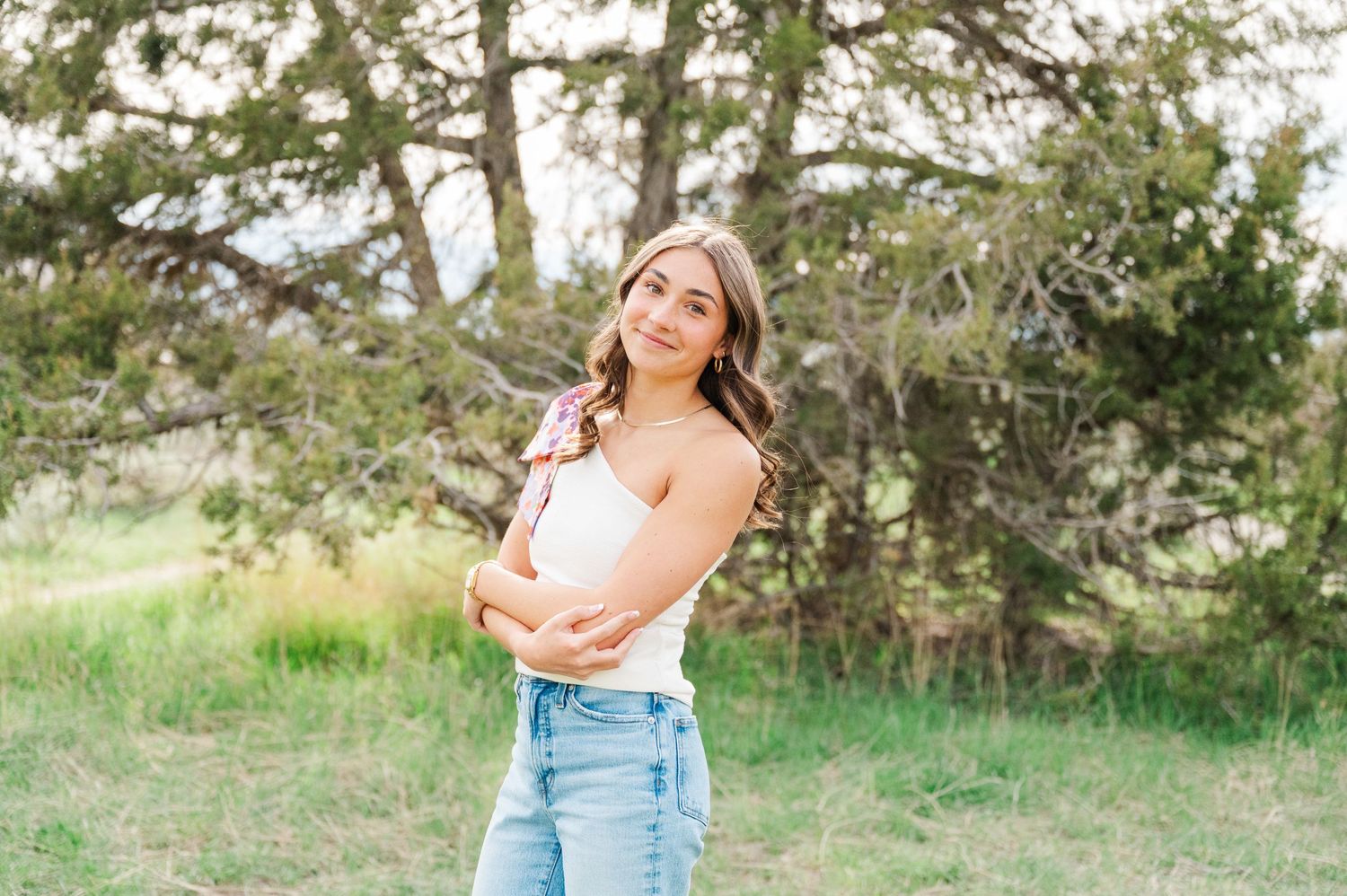 A young woman in casual attire poses outdoors against a natural backdrop of trees.