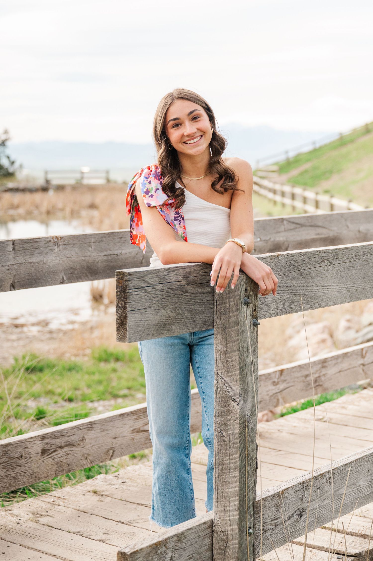 A woman in jeans and white top leans against a wooden fence on a sunny spring day.