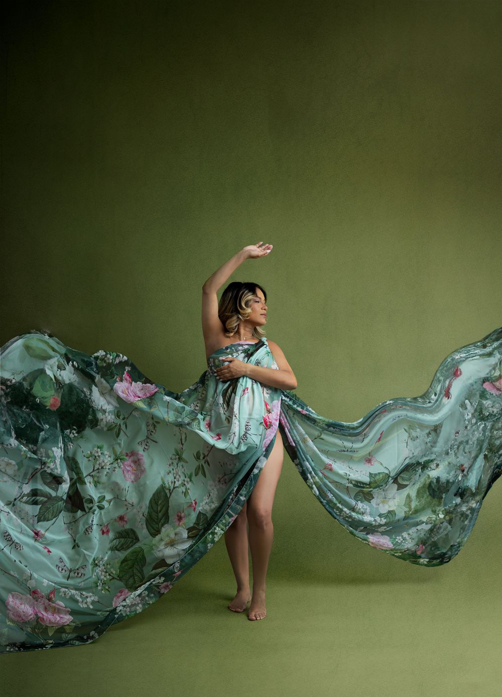 Dancer in flowing aqua dress performs graceful movement against green backdrop.