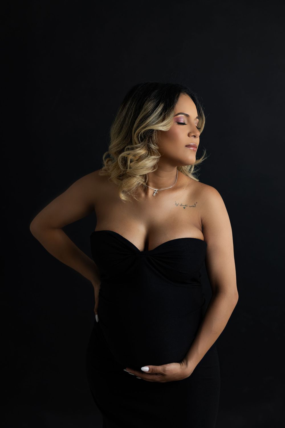 Elegant maternity portrait of woman in black dress against dark background.