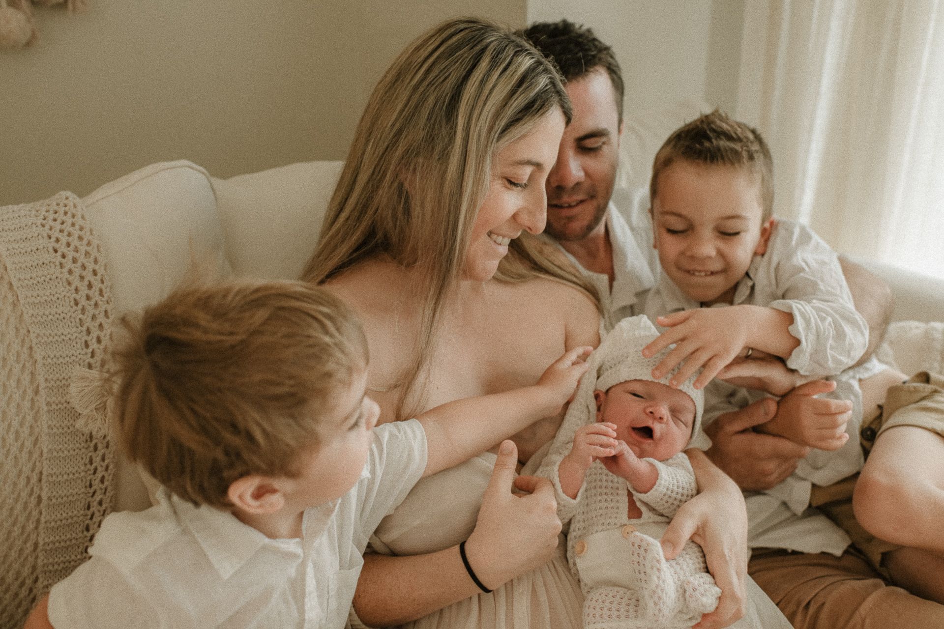 A tender family moment as they gather on a sofa to admire their newborn baby,  in a newborn studio located in southern Sydney.