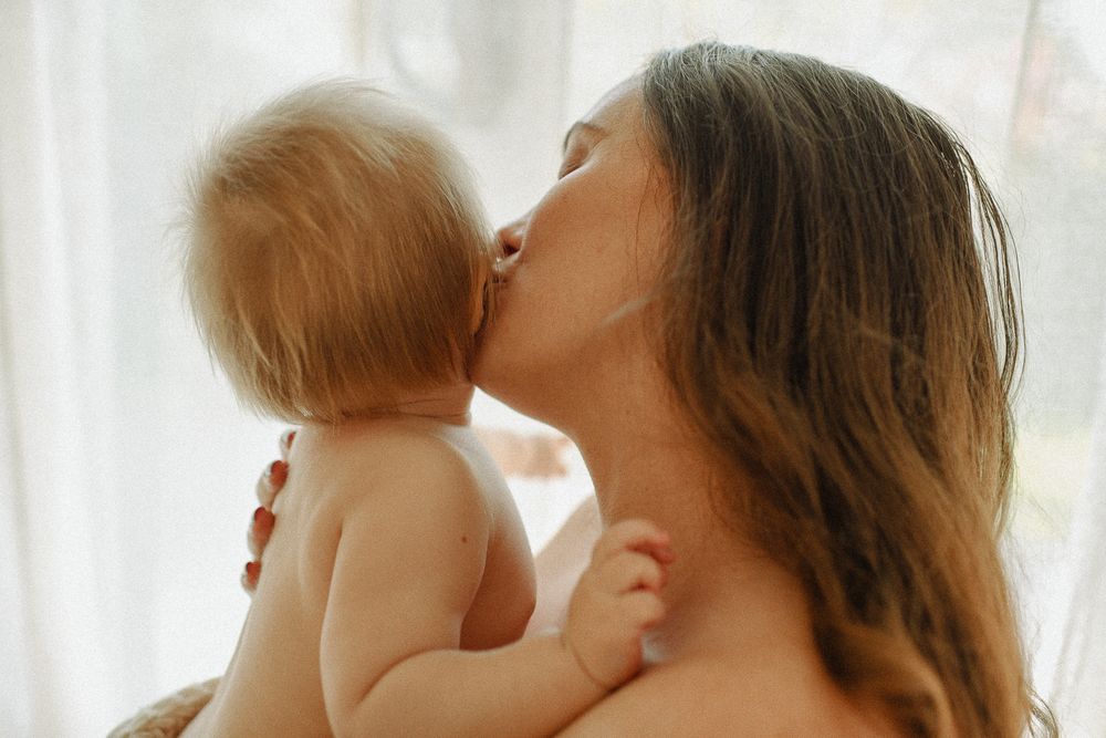 Intimate moment between parent and baby against soft white curtain backdrop.