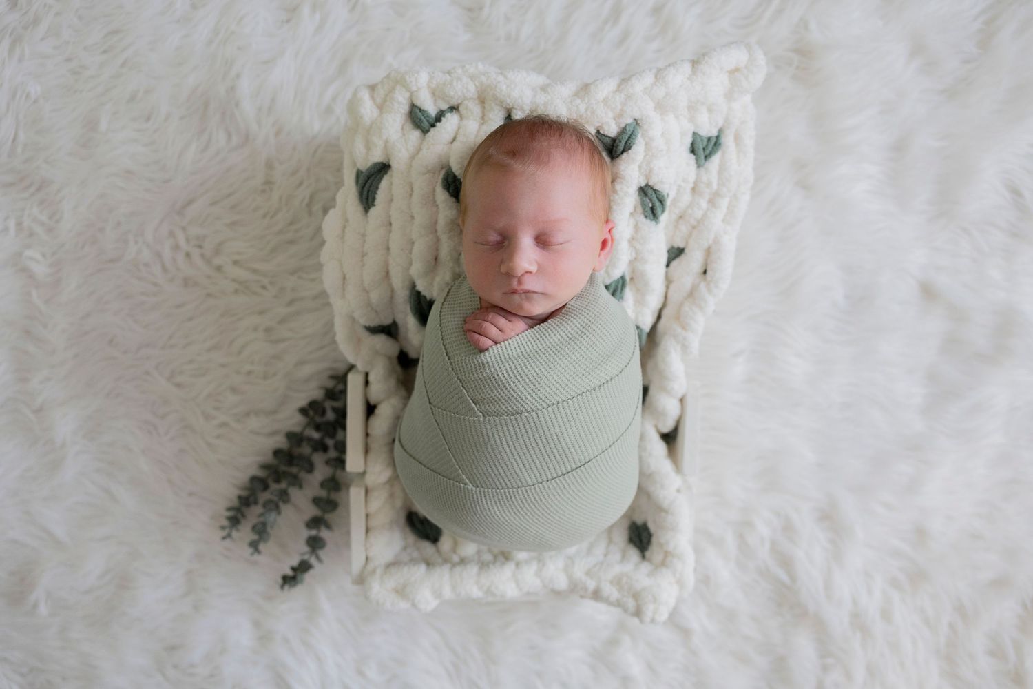newborn baby boy wrapped in potato in a green wrap in a basket by a Rochester Hills photographer