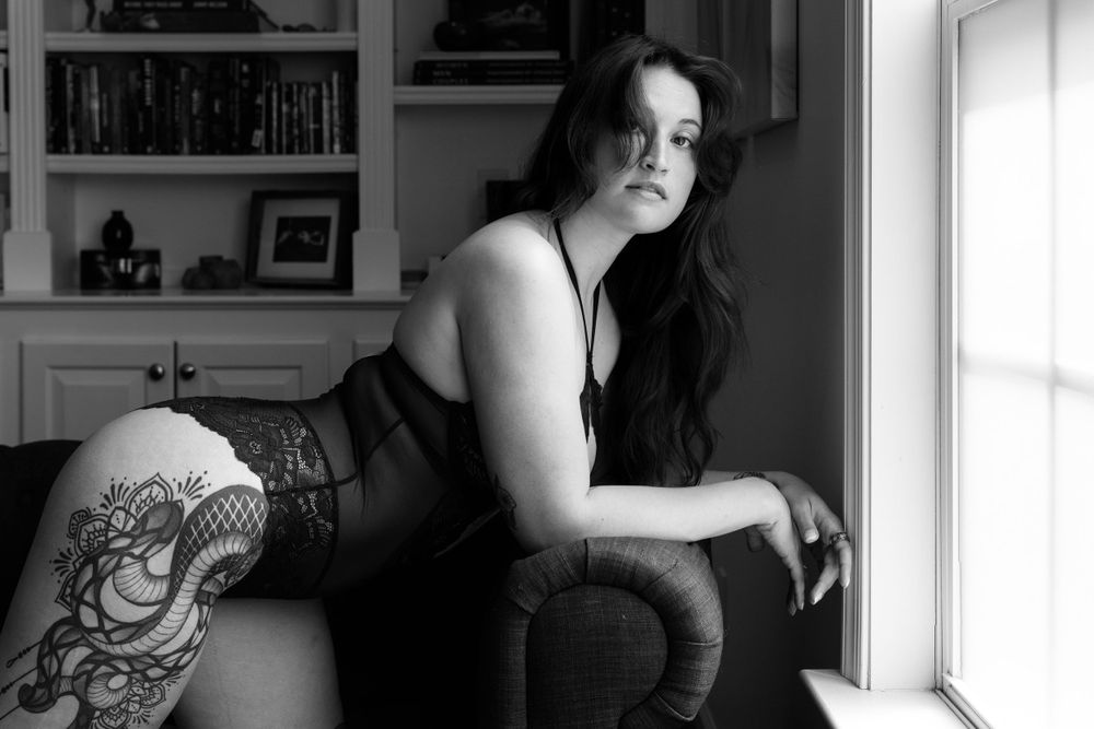 Boudoir photography session in black and white. Model has tattoos and leaning on the couch in Charlottesville, VA