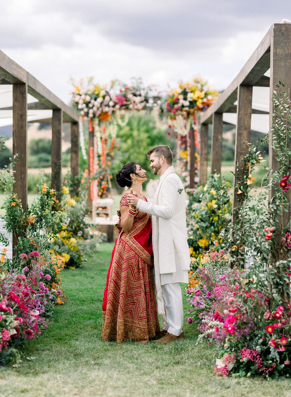 Wedding couple amid vibrant floral archway in outdoor garden setting.